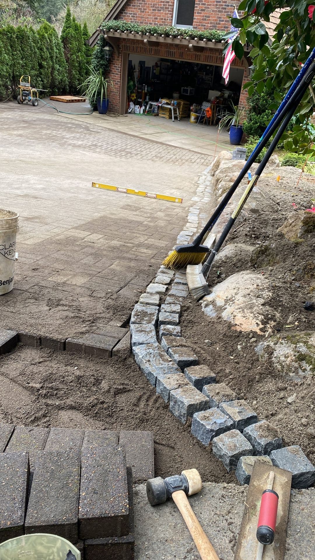 Curved paver edge being set in sand with mallet, level, and brooms