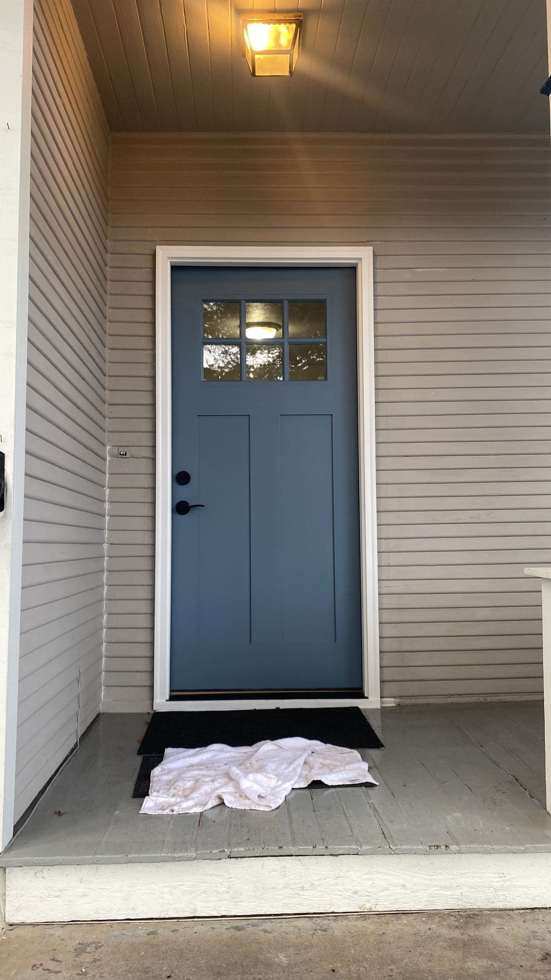 Finished blue-gray craftsman entry door with a six-lite window on a covered porch