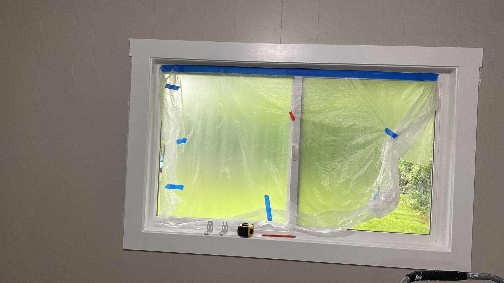 Freshly painted white window trim with the glass masked off in plastic