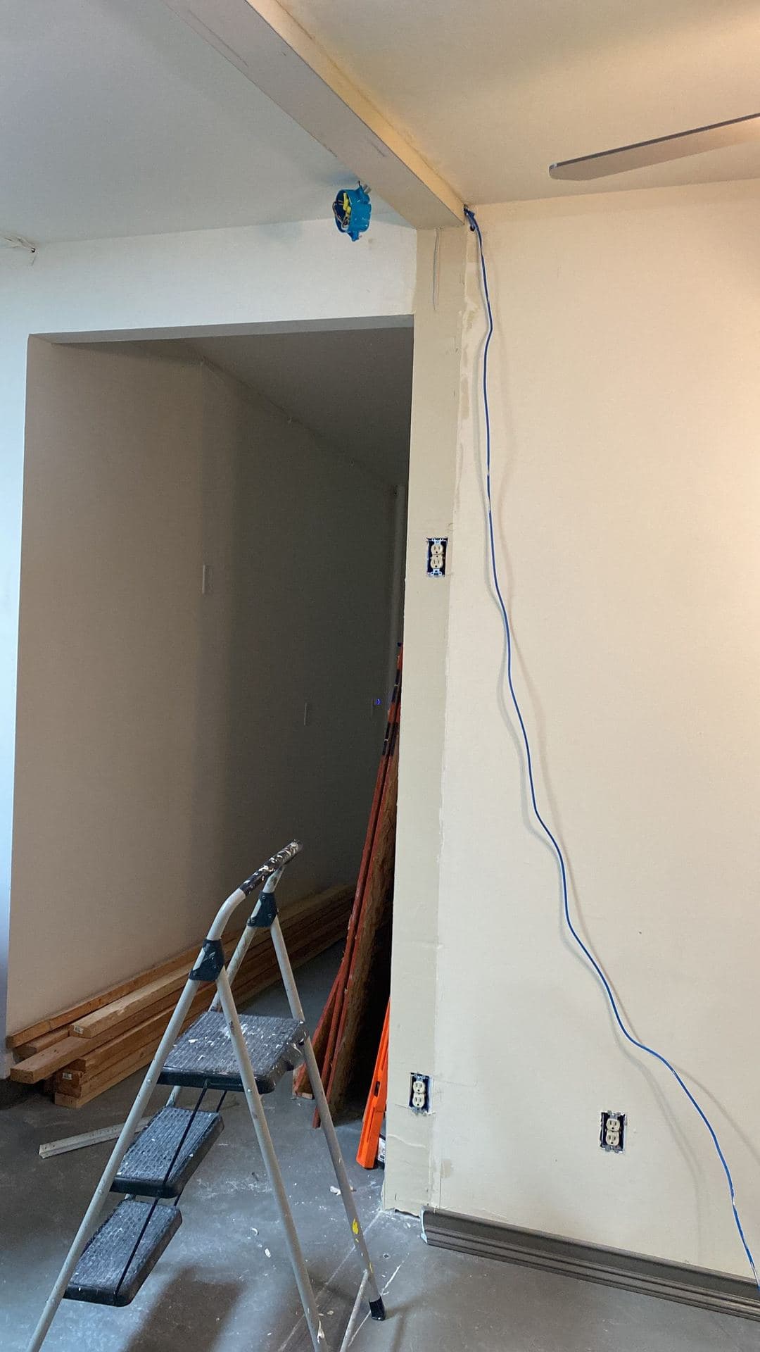 Interior remodel with stacked lumber, exposed wiring, and open outlet boxes