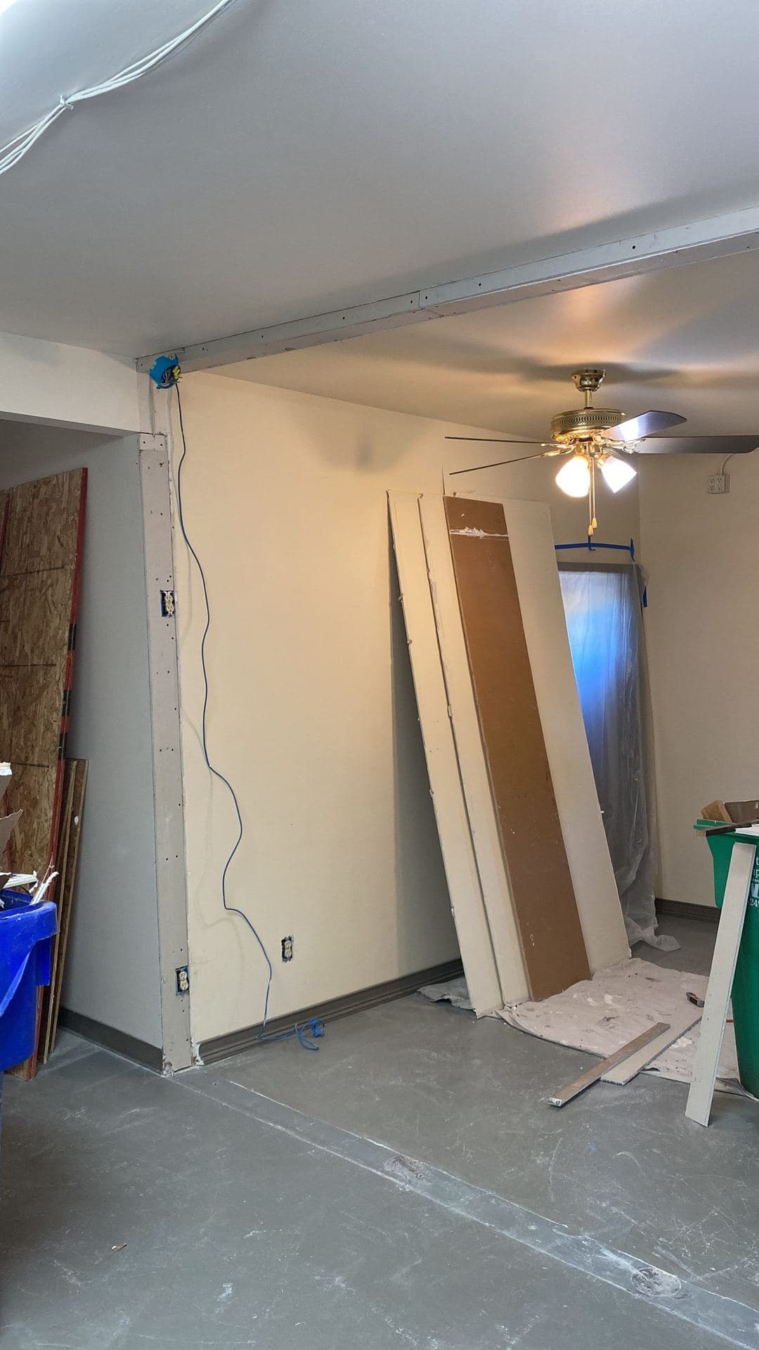Room mid-remodel with drywall sheets staged and exposed wiring