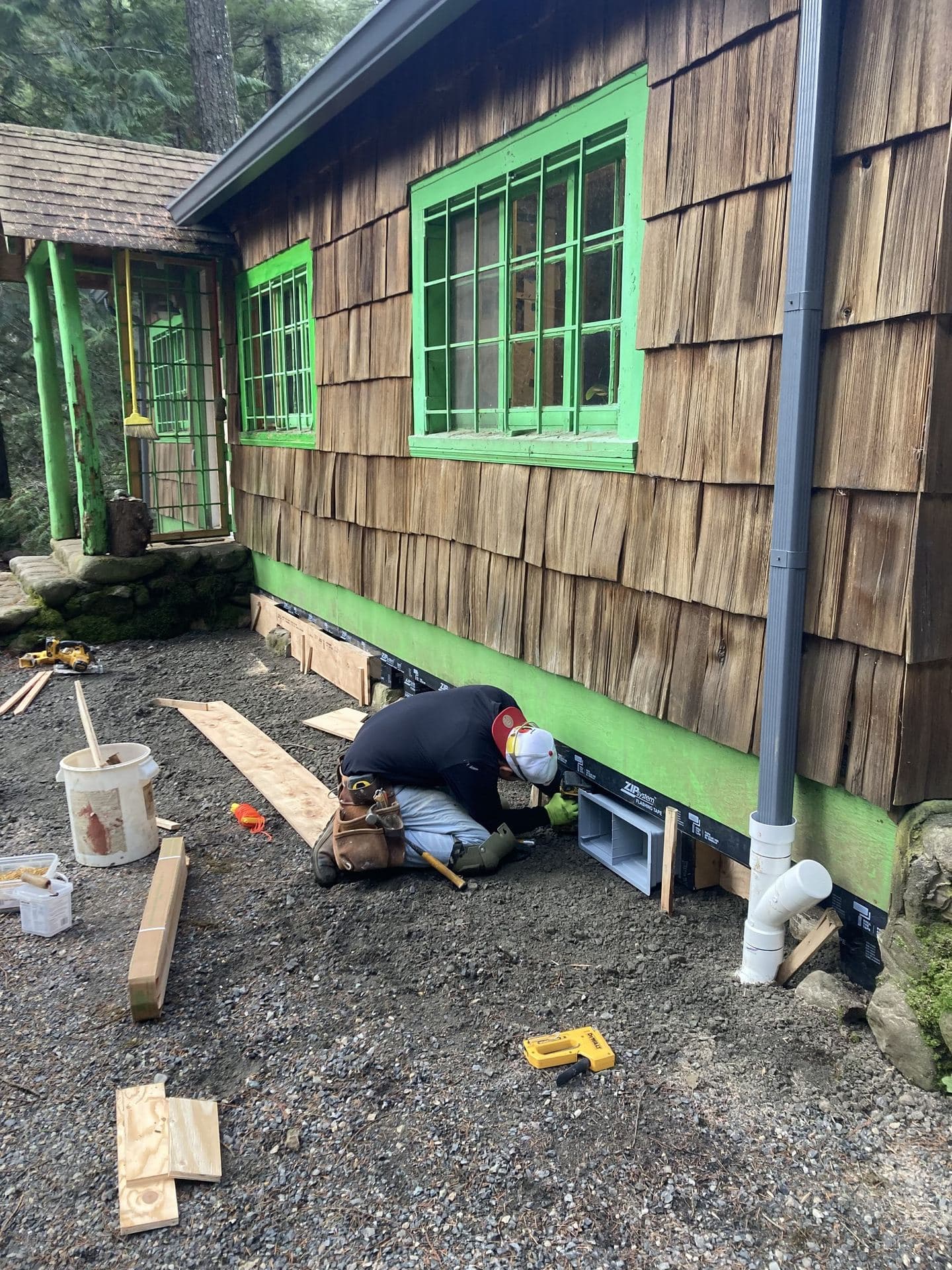 Cedar shingle siding being nailed at the base of a wall over green sheathing
