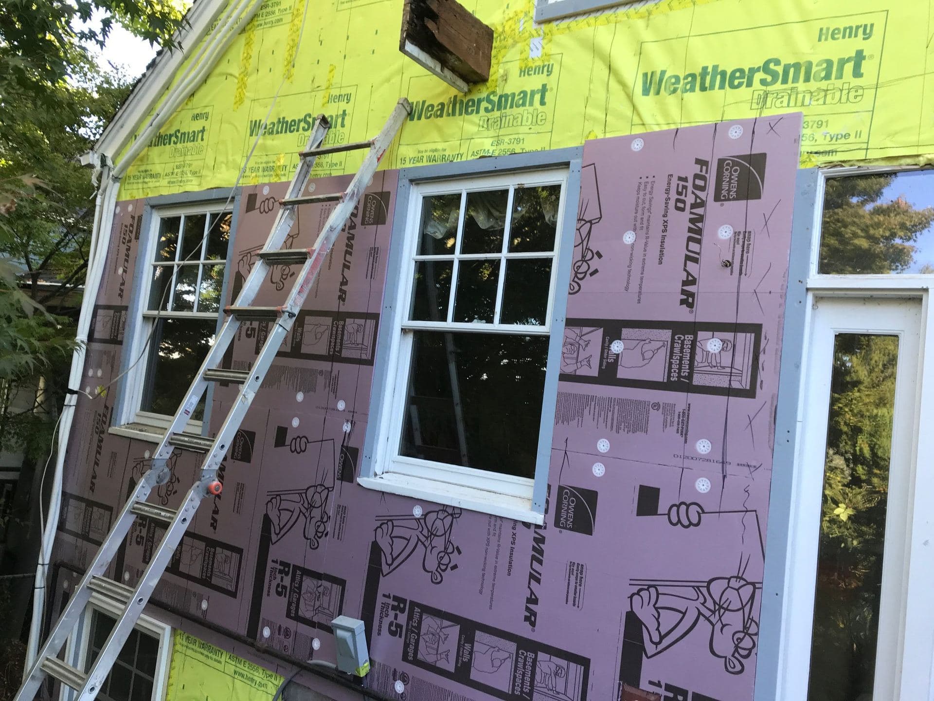 Exterior wall stripped to housewrap with foam insulation boards being installed